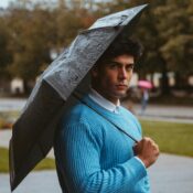 A young man in a blue sweater holds an umbrella on a rainy day in a Munich park.